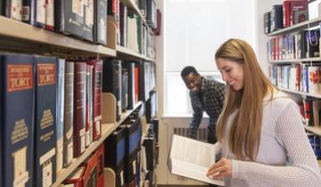 smiling students examining a book in the library stacks