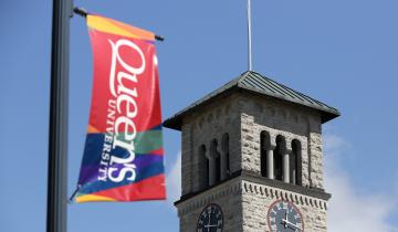 Image of the Queen's flag flying with the Grant Hall clocktower in the background