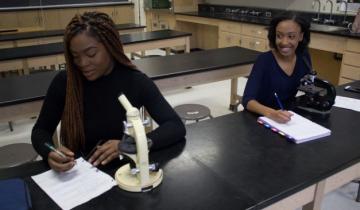 Two female students working in a lab with microscopes in front of them. 