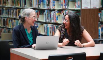 Brenda Reed laughing at a table alongside graduate student, Suparna