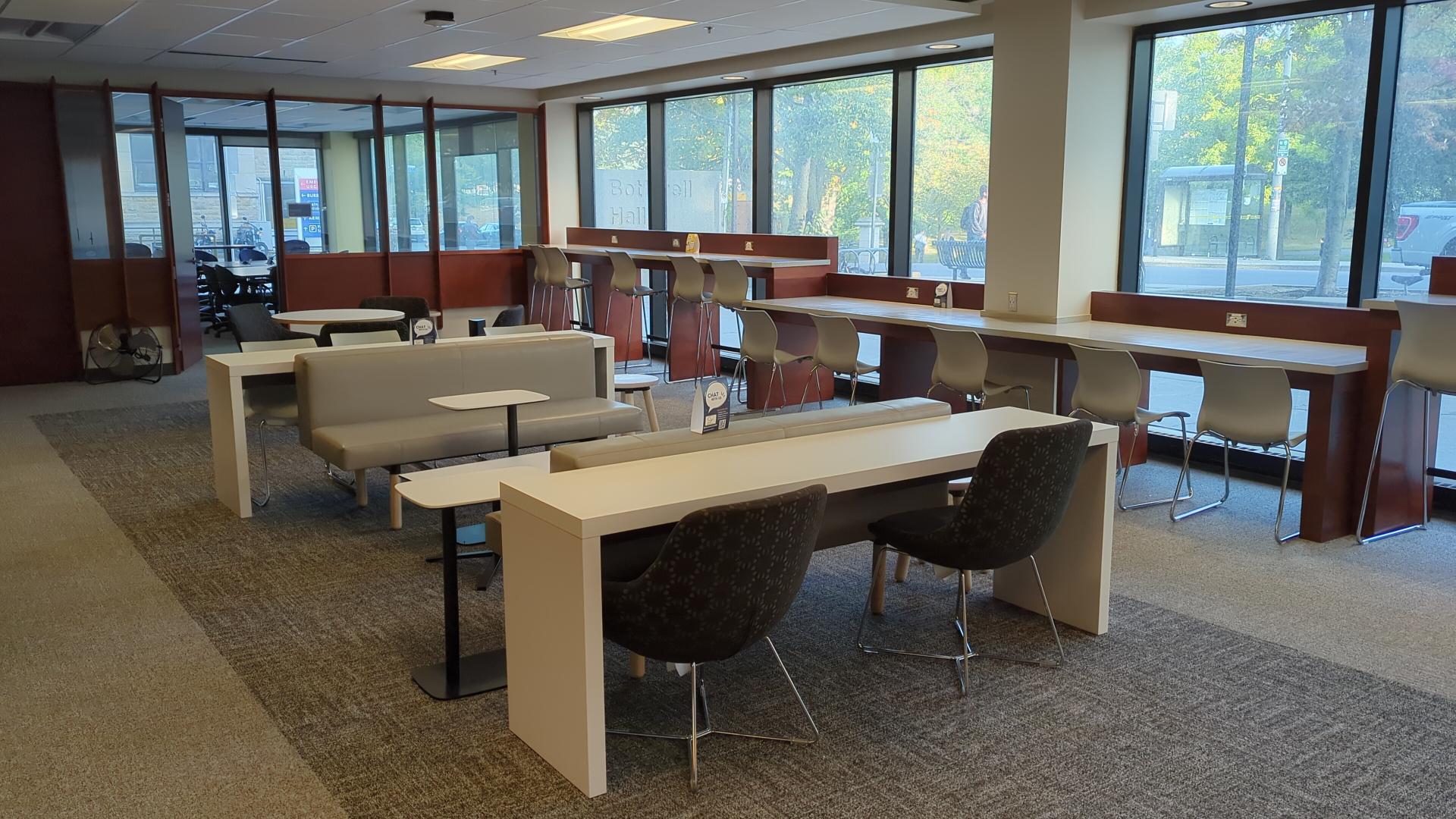 Study desks in center of photo with additional desks lining a window looking out to trees across the street