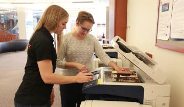 Two women operating the printing/copying machine.