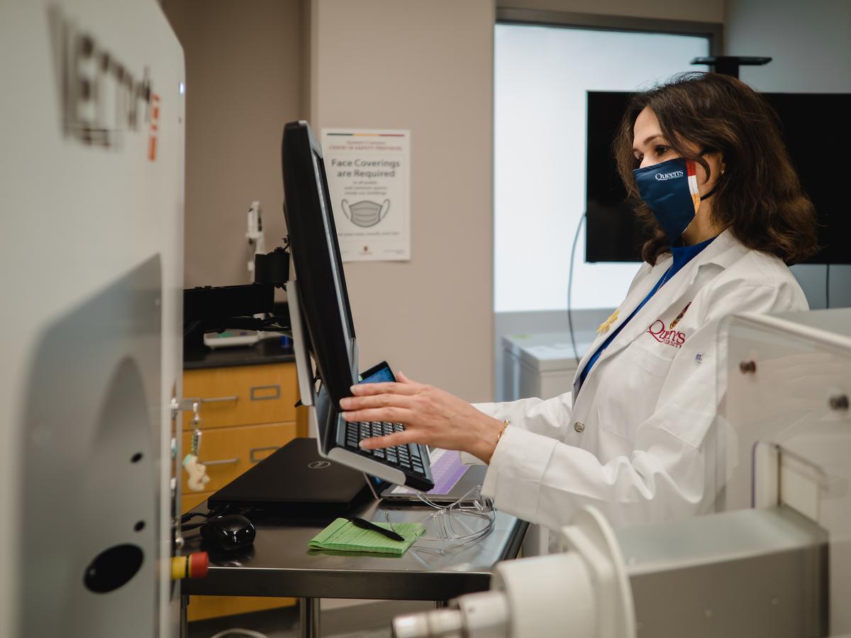 A woman wearing a mask and lab coat types at a computer