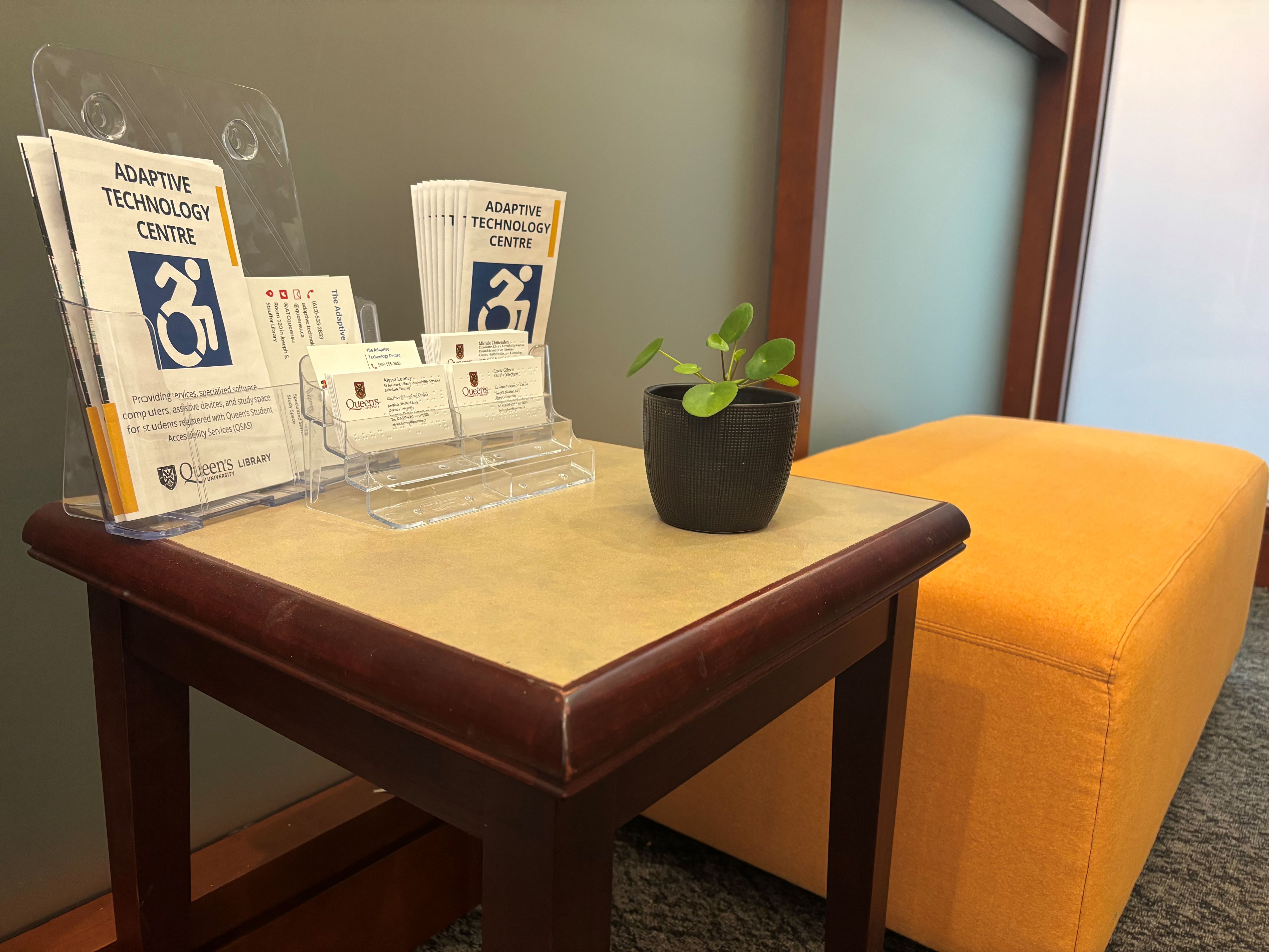 Adaptive Technology Centre brochures sit on a wood table next to an orange bench at the entrance of Stauffer Library room 119.