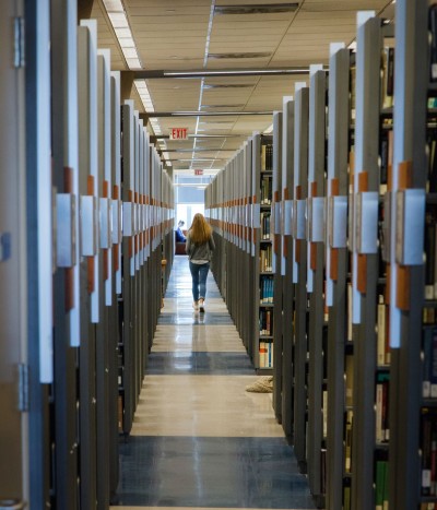 student walking between to rows of stacks in the library