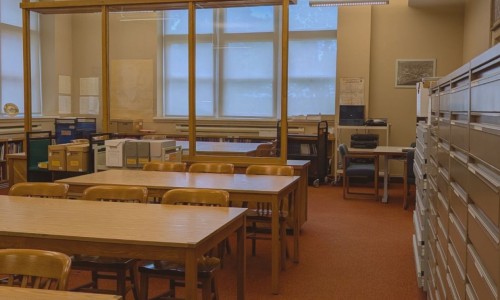 Queen's University Archives reading room. Two desks with three chairs each, filing cabinet, and fonds boxes.