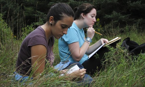 Two female students recording observations in notebooks in a field